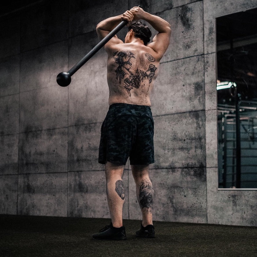 An athlete training with a steel mace beside a concrete wall